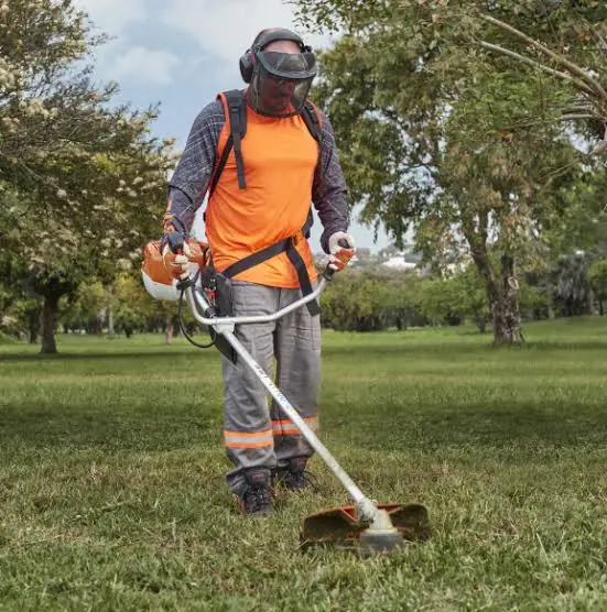 Operario con equipo de protección individual utilizando una desbrozadora en un parque